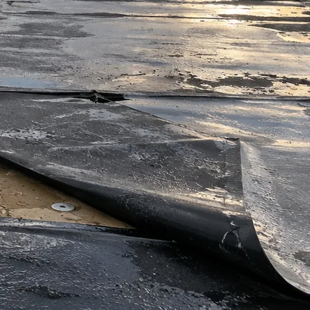 Close view of membrane peeled back from the roof edge after a storm